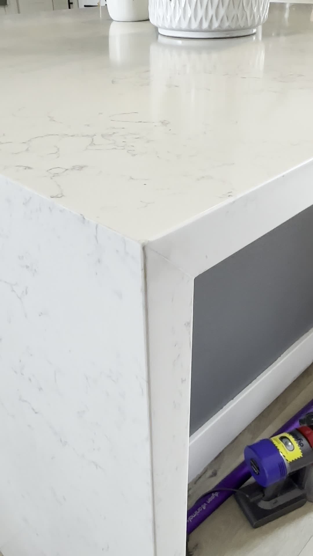 Mitered waterfall corner of a marble-look quartz countertop over a gray cabinet panel