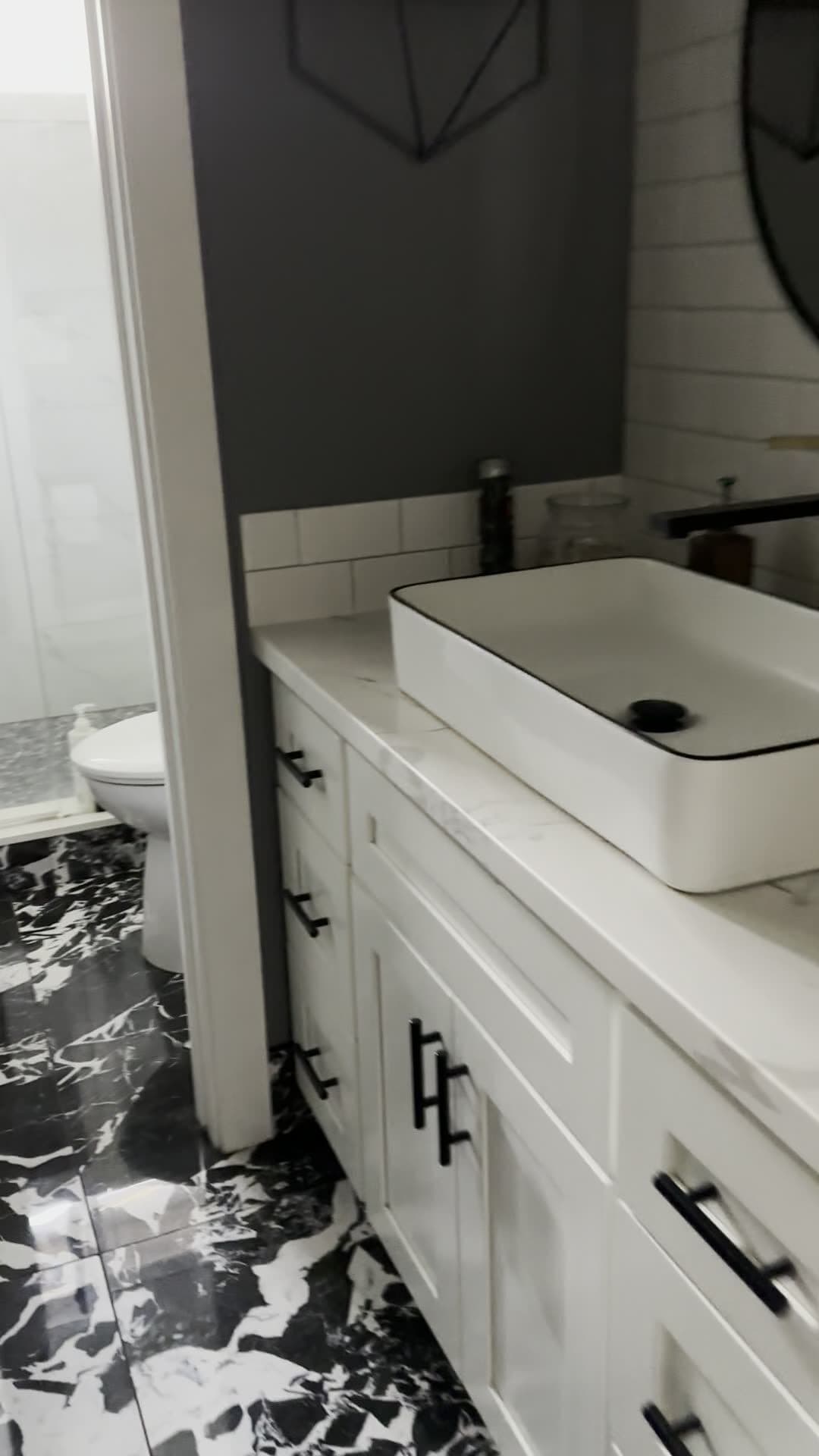 Bathroom vanity with marble-look quartz top and black-rimmed vessel sink, black-and-white marble-look tile floor, and glass shower door
