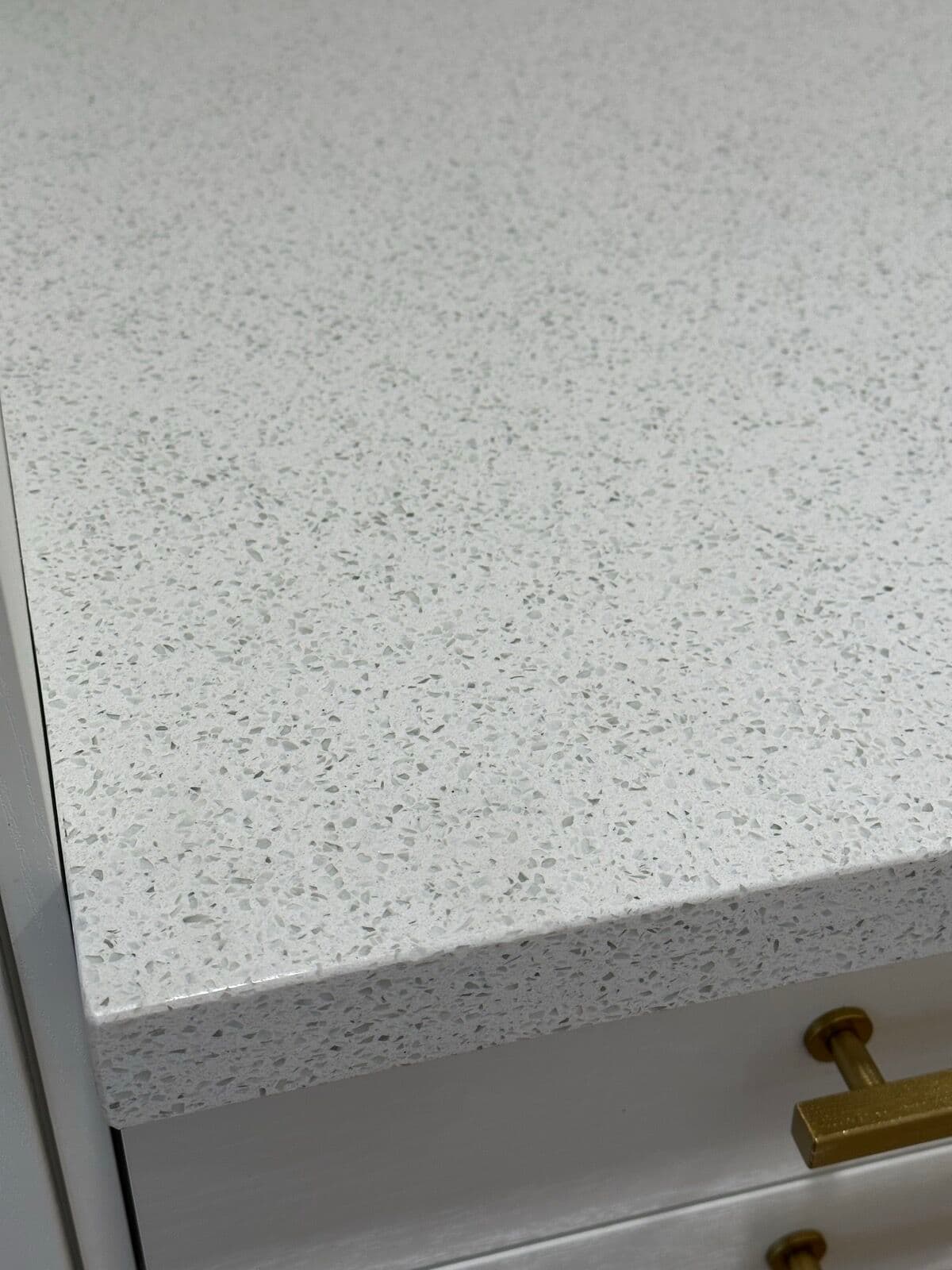 Closeup of a sparkle-white quartz countertop edge above a cabinet drawer with a brushed brass pull