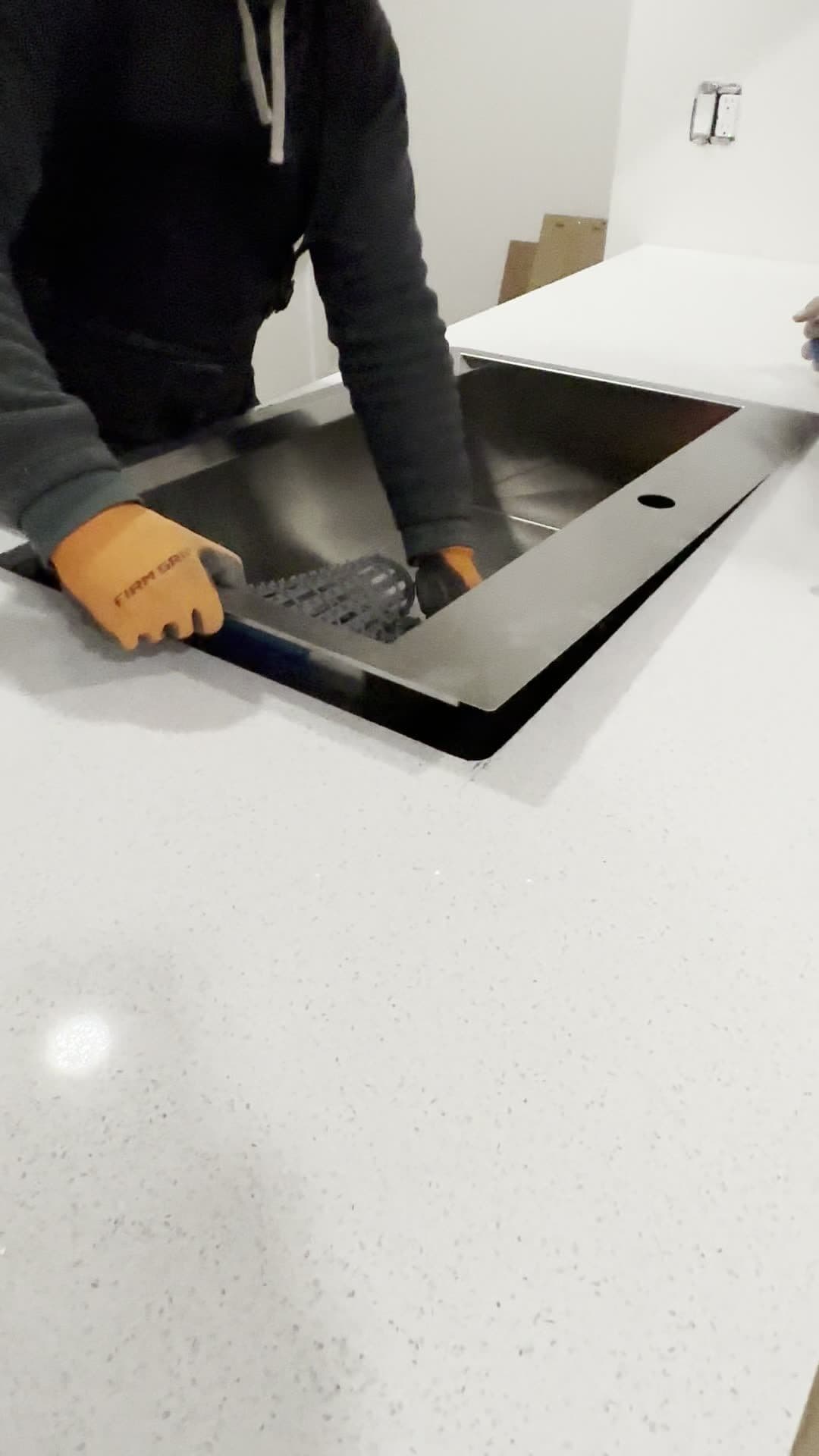 Gloved hands lowering a black stainless sink into a cutout in a white quartz countertop