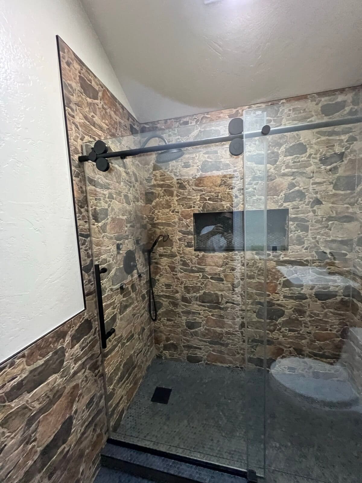 Stone-look tile shower walls with recessed niche, black rain shower head, and glass sliding door