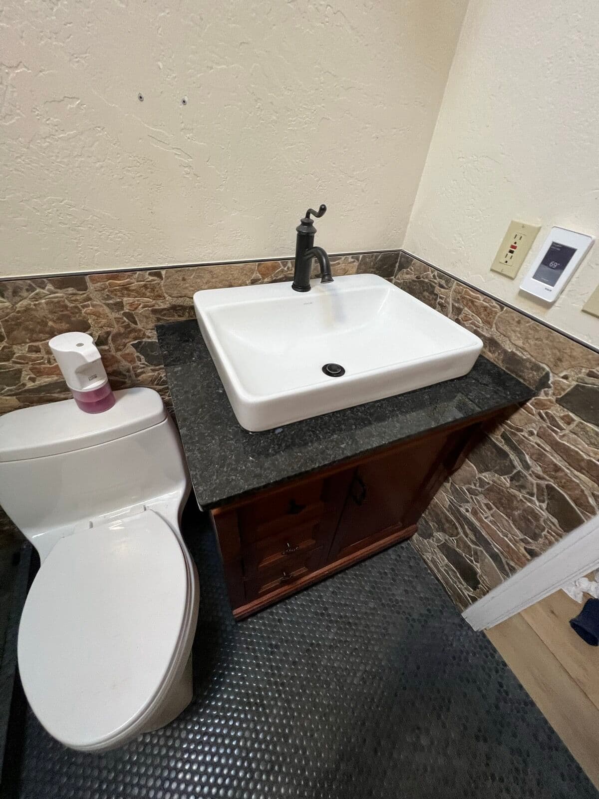 Dark wood vanity with black granite-look top, white sink, oil-rubbed bronze faucet, and stone-look wainscot tile