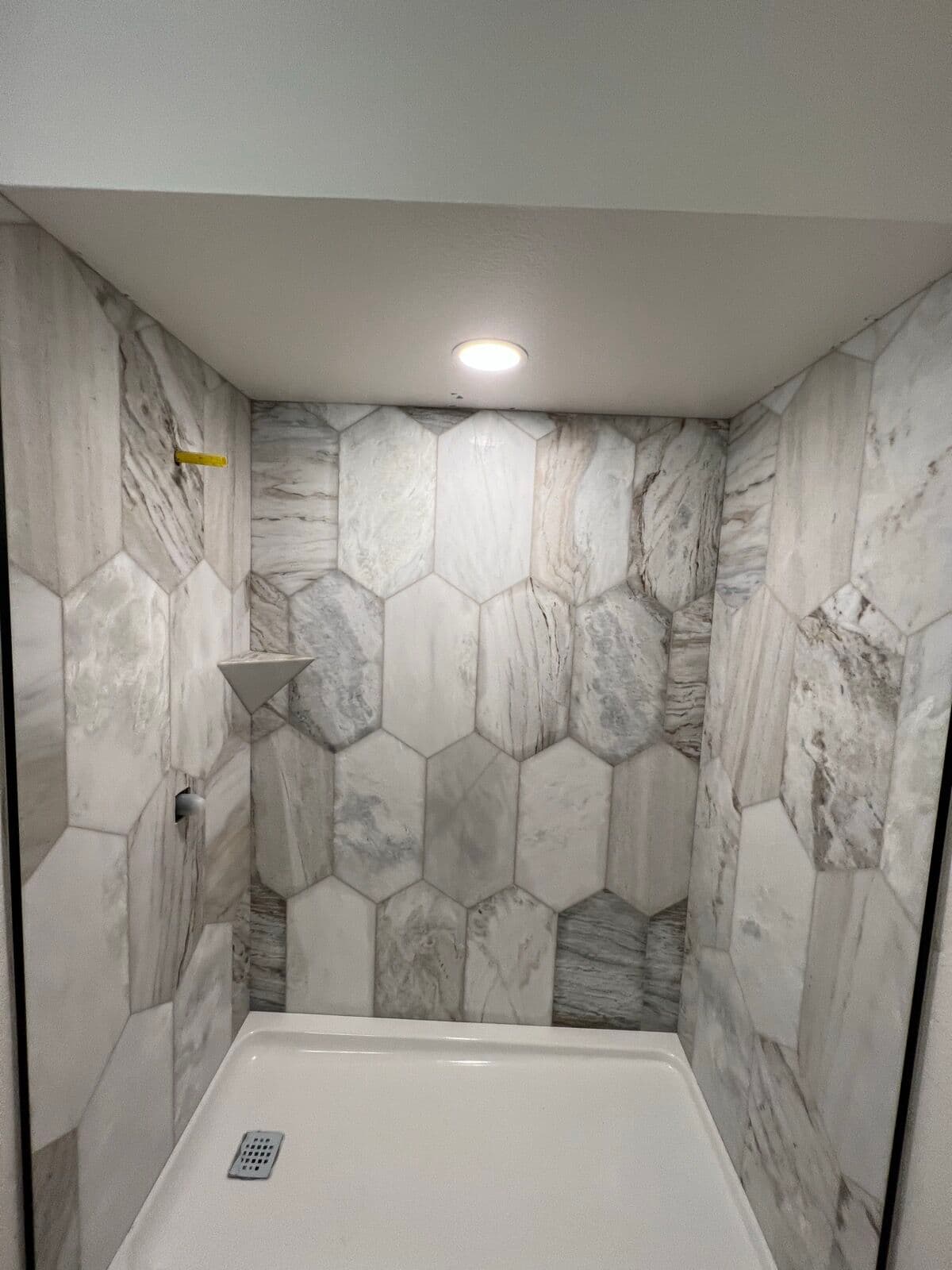 Shower walls in elongated hex marble-look tile with a corner shelf and white shower pan