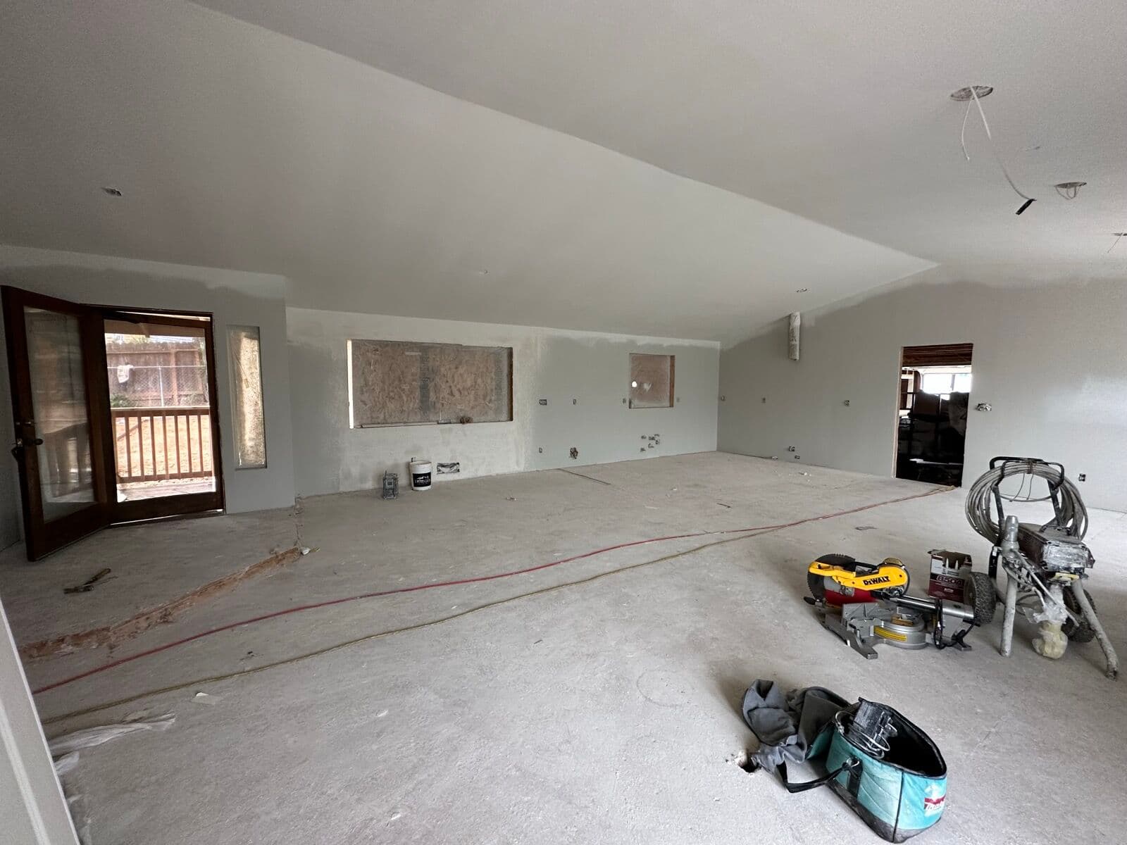 Vaulted great room at the drywall and primer stage with a paint sprayer, miter saw, and open French doors