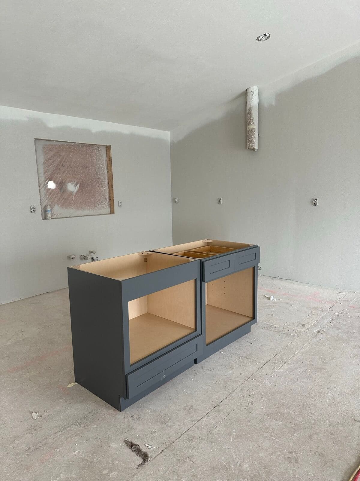 Charcoal-gray shaker base cabinets set on a bare concrete slab in a drywalled room