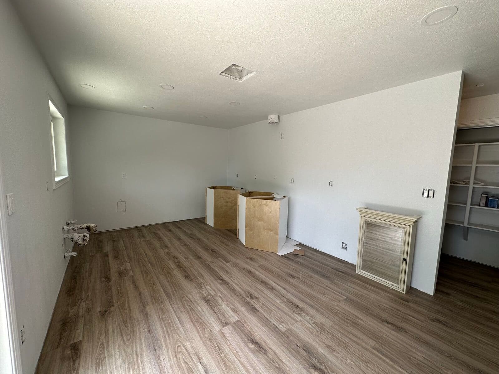 Empty room with new wood-look vinyl plank flooring and unfinished cabinet boxes staged along the wall