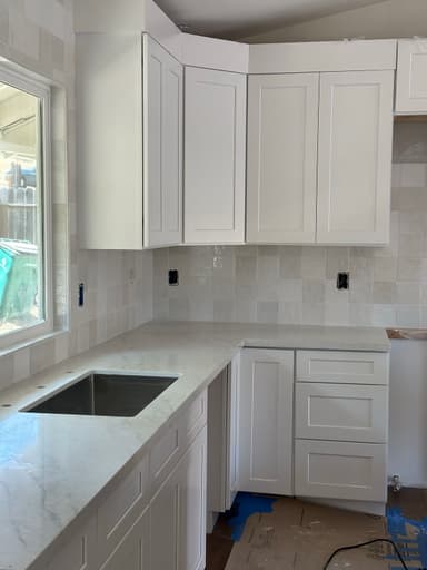Kitchen corner with white shaker cabinets, marble-look countertop, undermount stainless sink, and glossy square tile backsplash