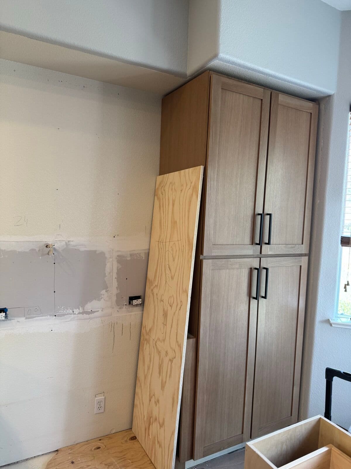 Tall white oak pantry cabinet installed against patched drywall during the remodel