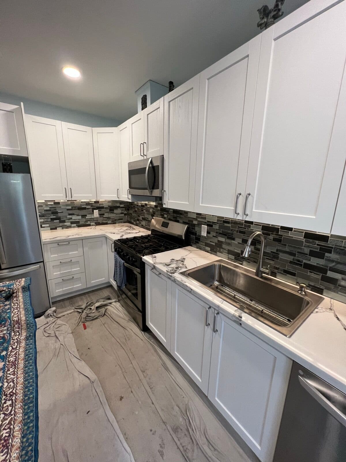 Kitchen with white shaker cabinets, marble-veined countertop, gray glass mosaic backsplash, and stainless sink