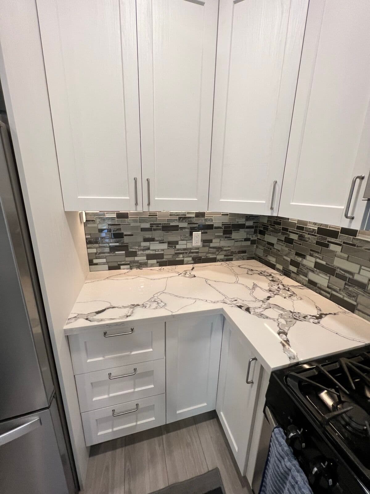 Corner countertop with heavy gray marble veining under white upper cabinets and mosaic backsplash