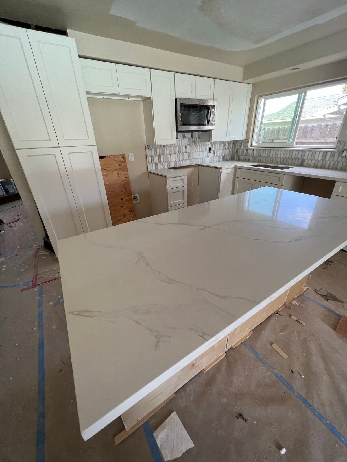 Large marble-veined island countertop slab set on its base in a cream shaker kitchen under construction