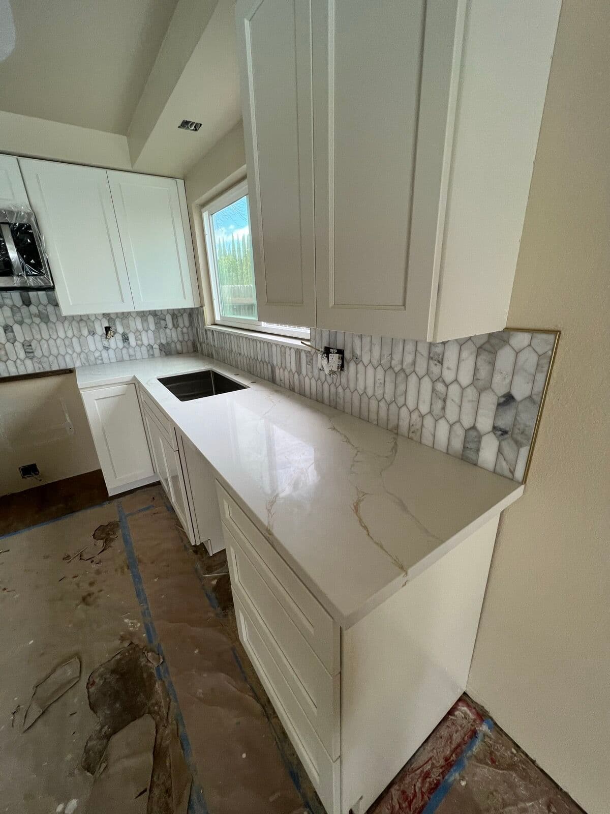 White countertop and undermount sink with marble picket tile backsplash finished with brass edge trim