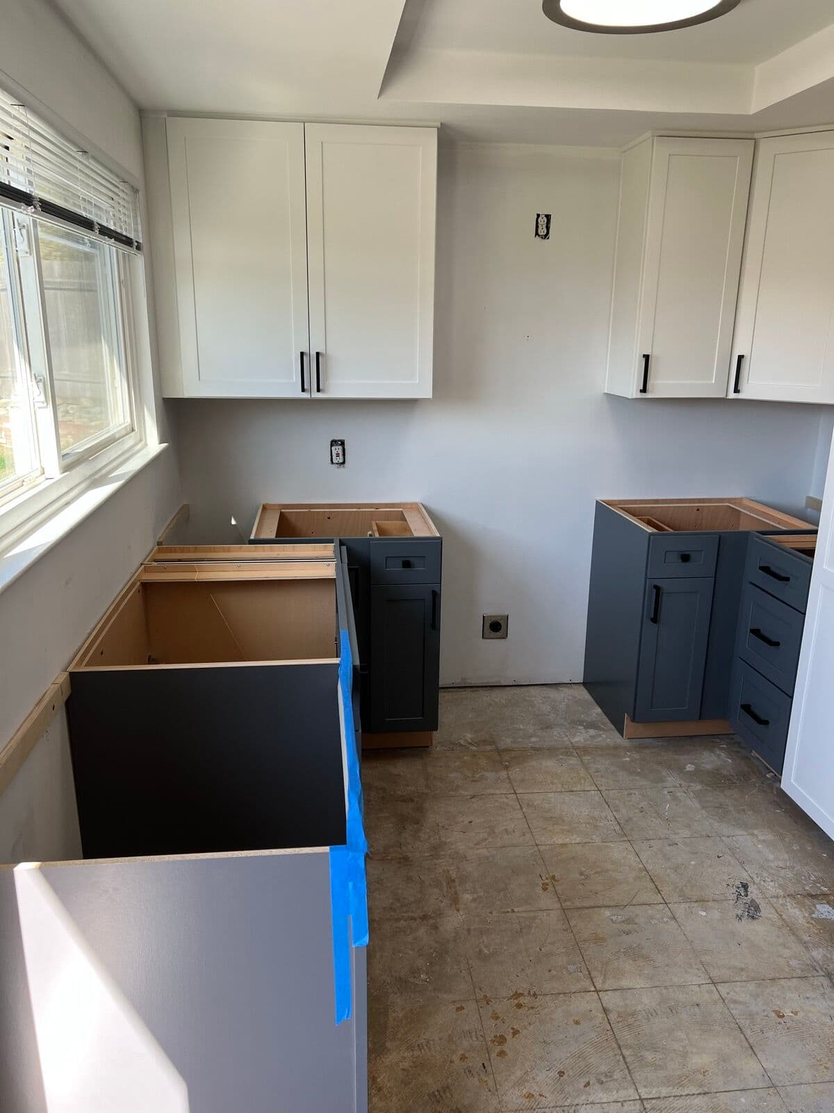 Slate-gray base cabinets and white uppers installed in a kitchen before countertops, old floor exposed