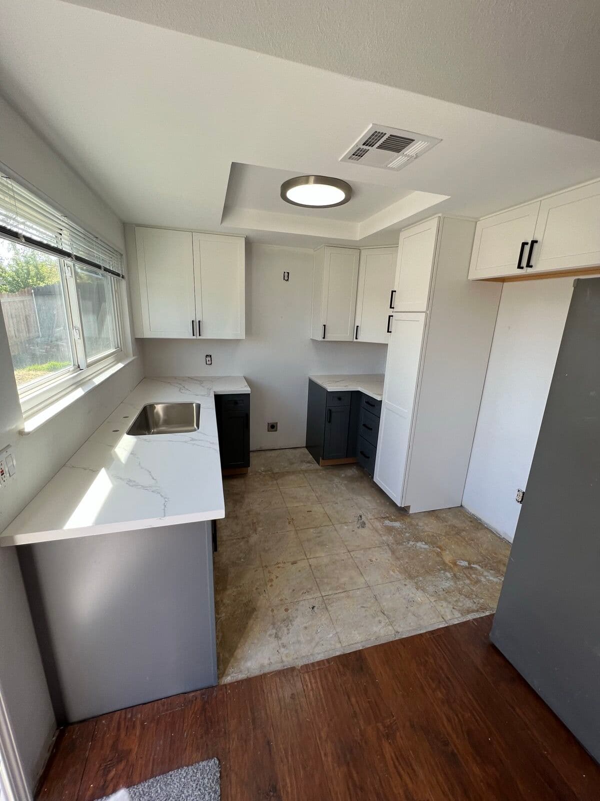 Two-tone kitchen with white upper cabinets, slate-gray base cabinets, and white countertops, floor not yet finished