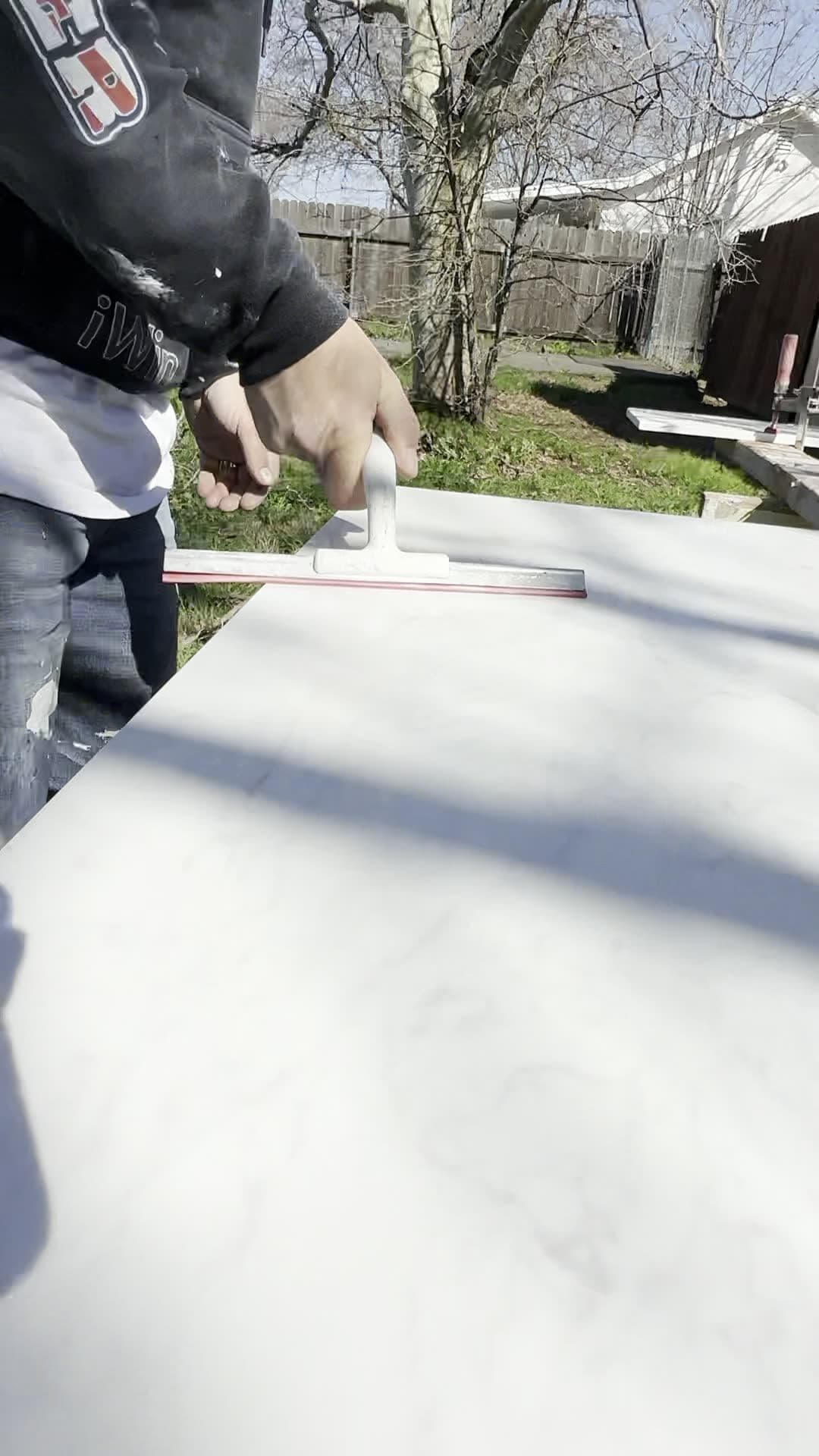 Worker spreading adhesive across a white marble-look panel set up outdoors