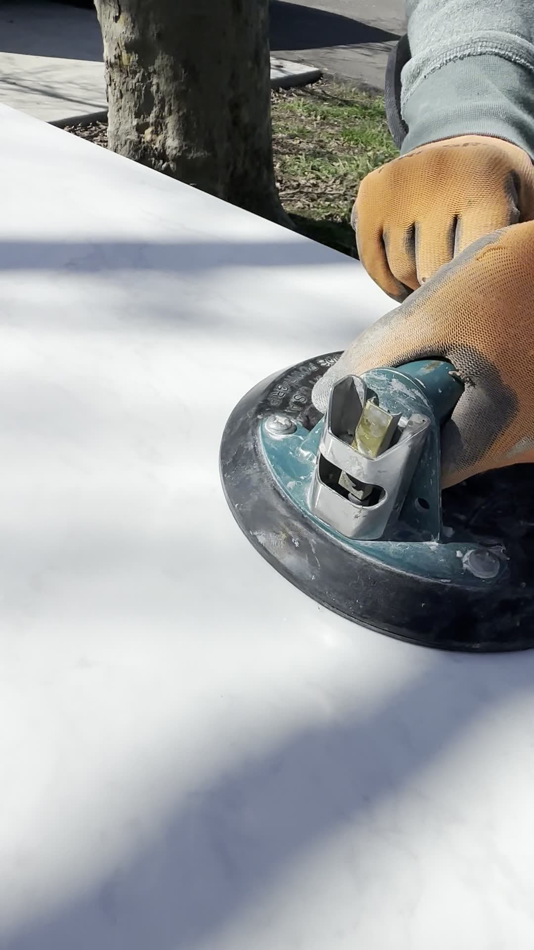 Gloved hands gripping a vacuum suction lifter on a white marble-look panel