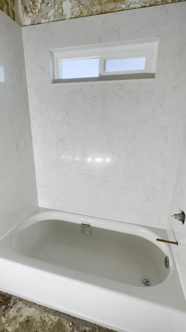 New white marble-look surround panels around an alcove bathtub with a small horizontal window
