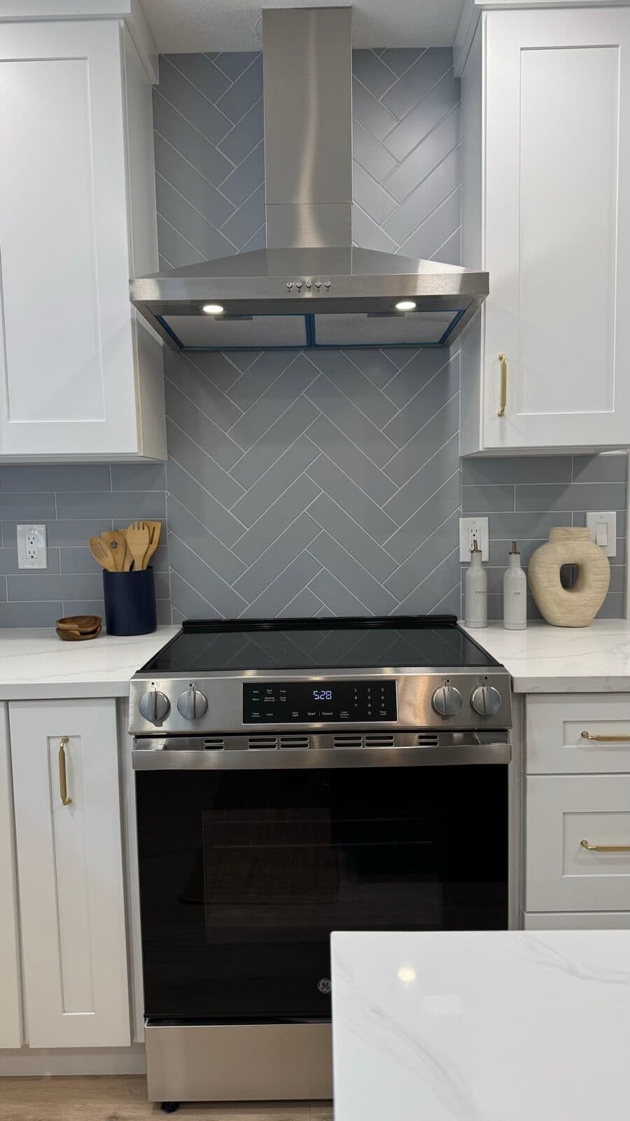 Stainless chimney range hood over an electric range with gray herringbone tile backsplash