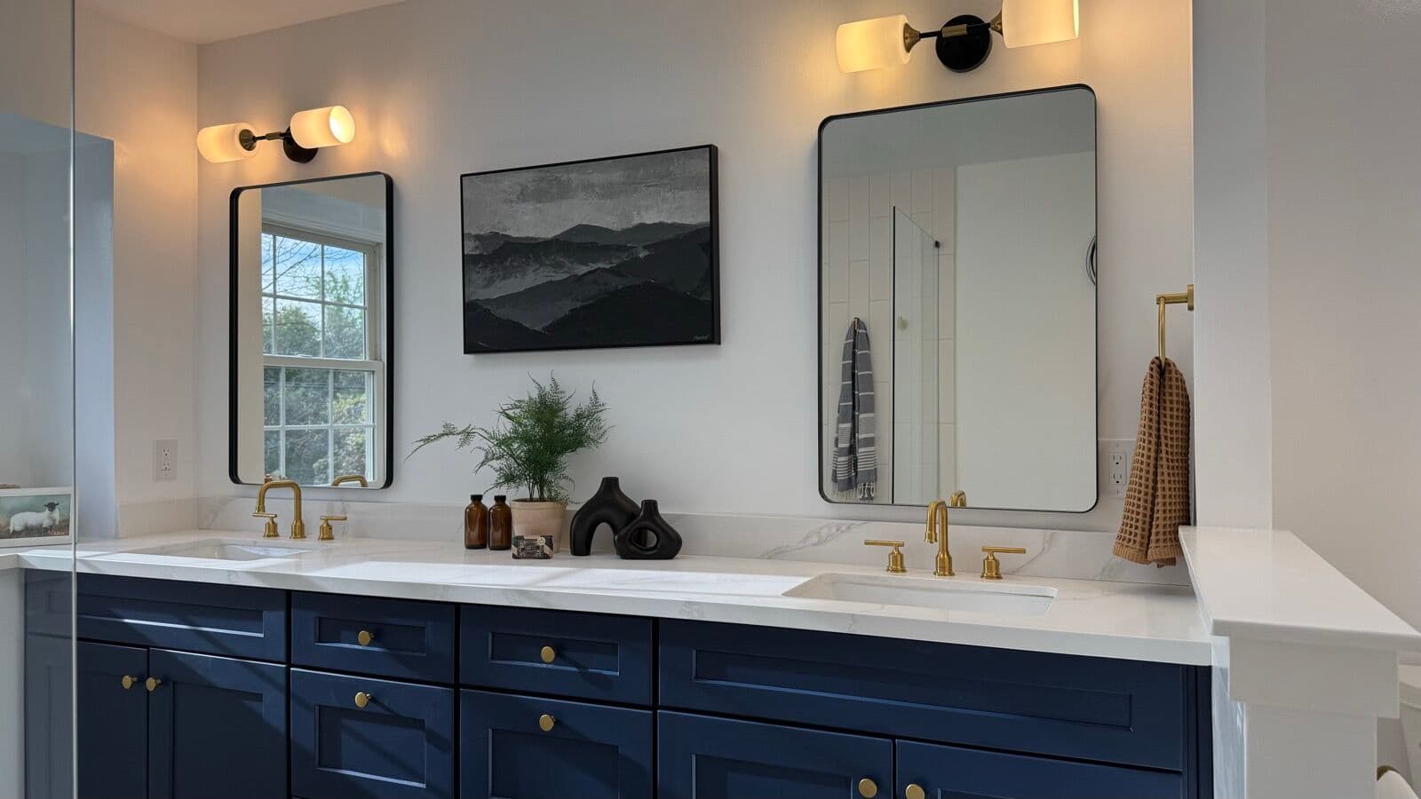 Primary bathroom double navy vanity with brass faucets, two black-framed mirrors, and sconce lighting