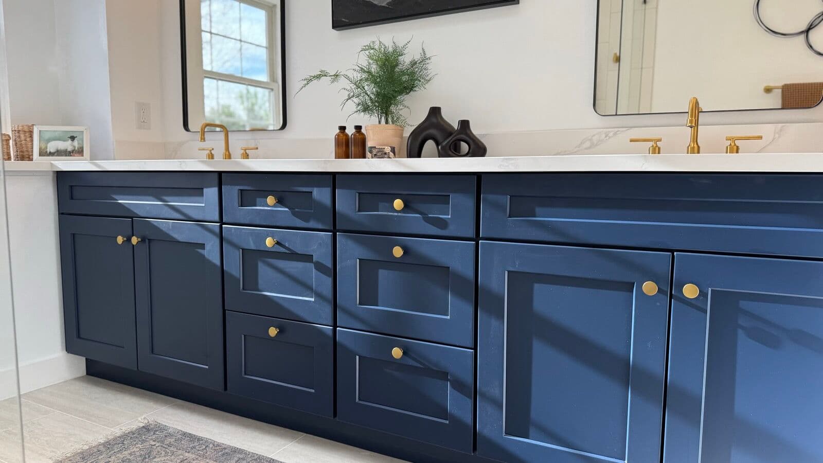 Close view of navy shaker vanity drawers and doors with brass knobs under a white countertop