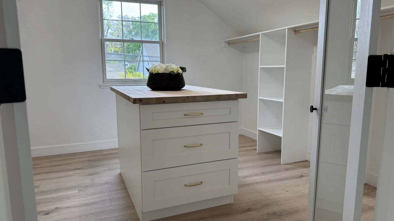 Walk-in closet with white island dresser, open shelving, hanging rods, and a bright window