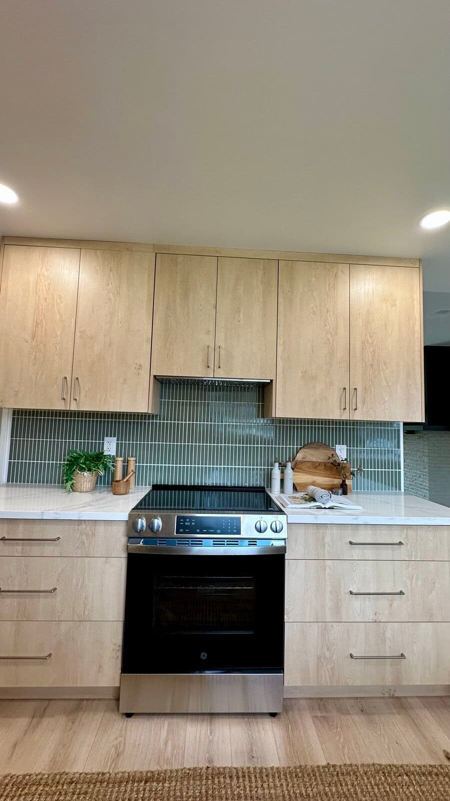 Stainless slide-in range flanked by white-oak cabinets with a sage-green vertical stacked tile backsplash