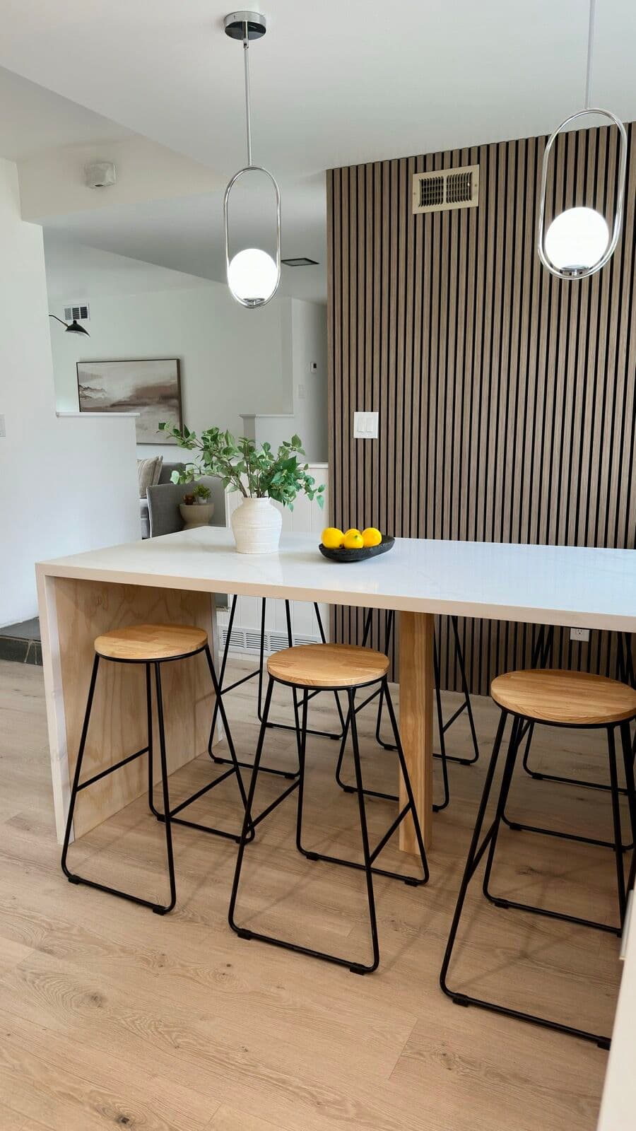 Quartz bar top with three wood-seat stools in front of a floor-to-ceiling wood slat accent wall