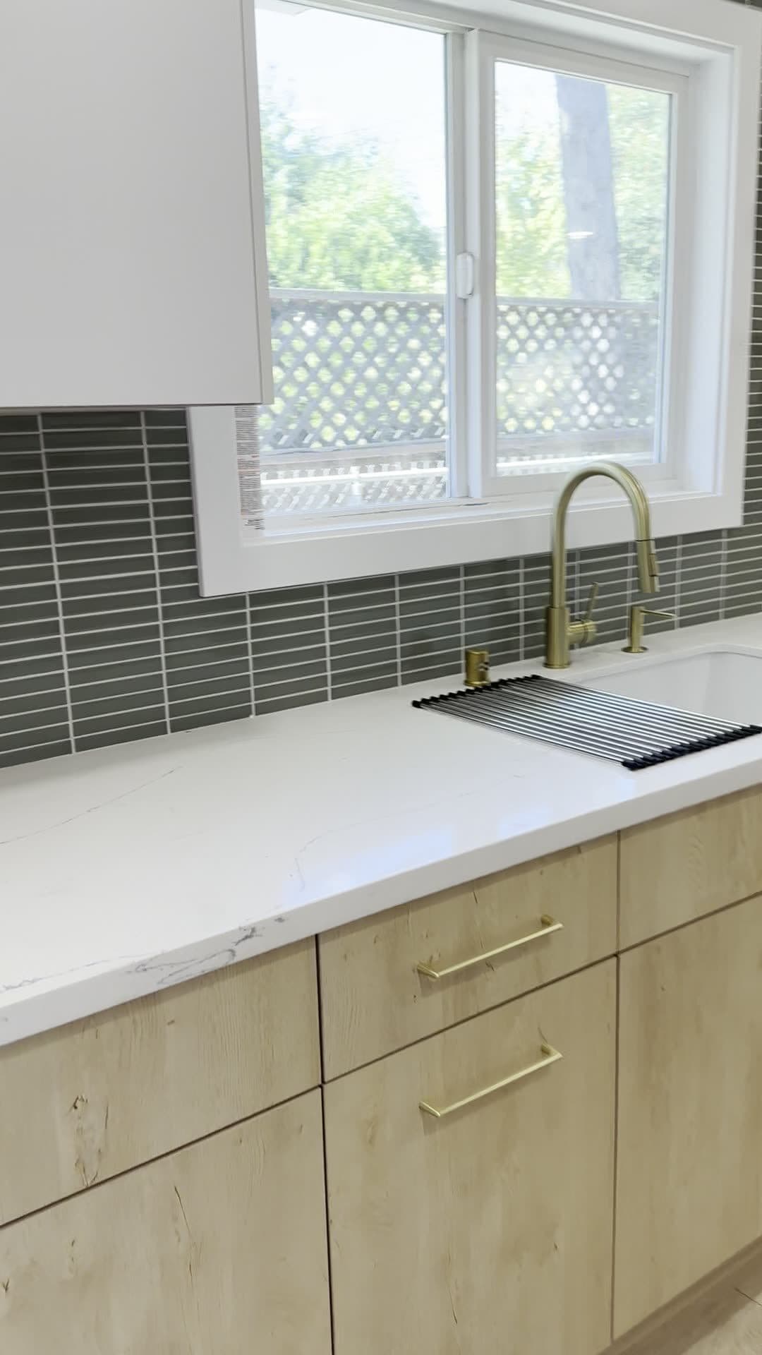 Close view of the brass faucet, undermount sink, and veined quartz-look countertop in front of the kitchen window