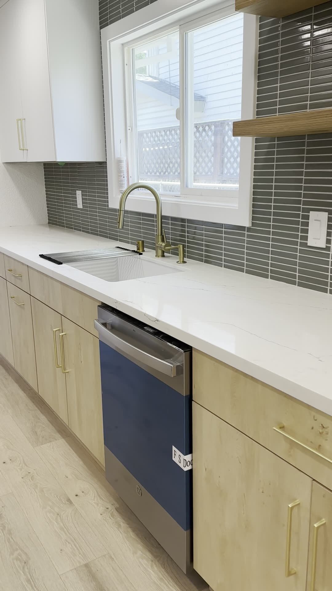 Kitchen sink run with brass gooseneck faucet, undermount sink, veined white counter, and gray-green stacked tile around the window