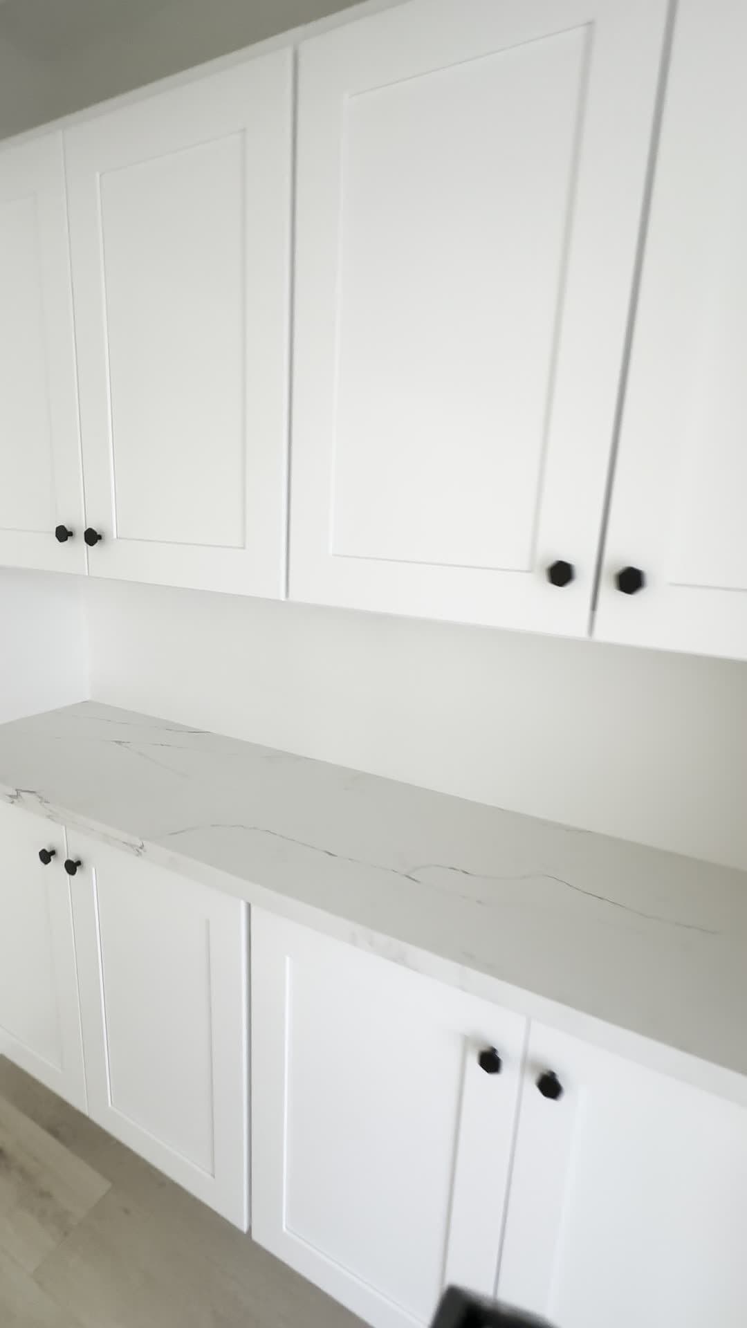 Built-in white shaker cabinets with black hexagonal knobs and a marble-look countertop along a pantry wall