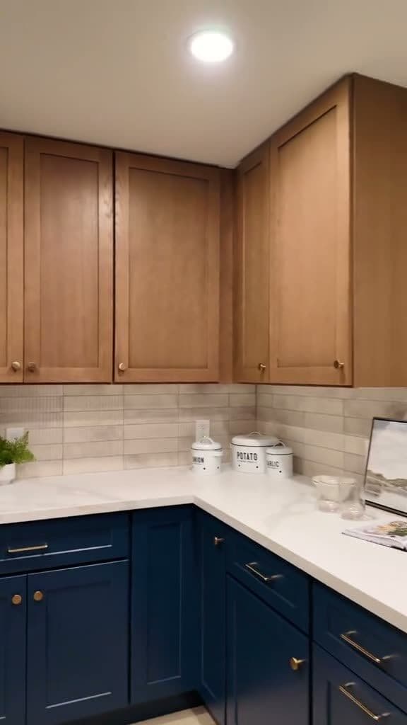 Corner cabinet run with white-oak upper cabinets, navy lowers, brass hardware, and white quartz-look countertop
