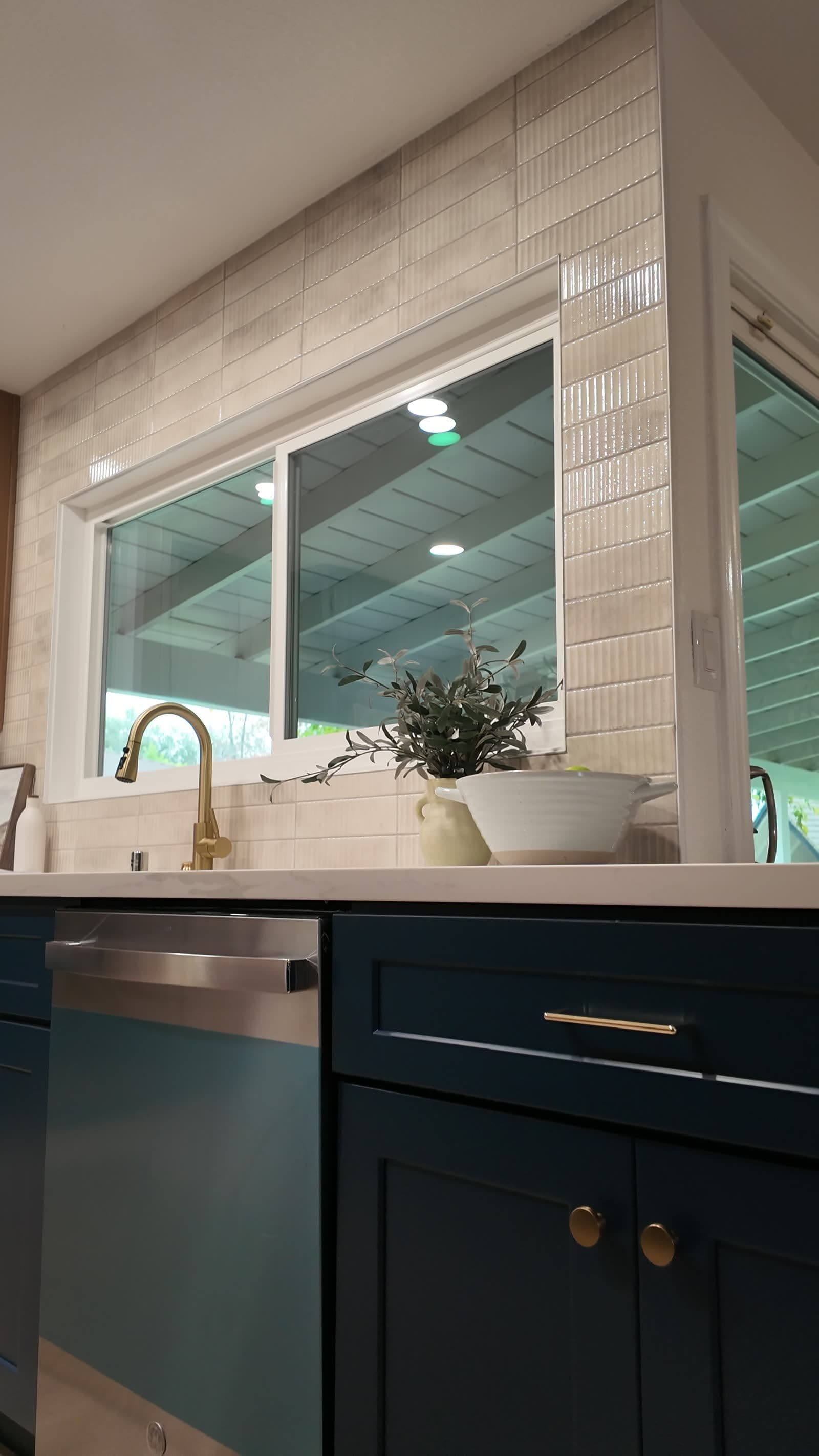 Sink wall with brass gooseneck faucet, fluted tile surround, and a pass-through window
