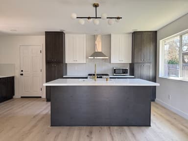 Kitchen island with dark cabinet base, white marble-look quartz top, and brass faucet under a globe chandelier