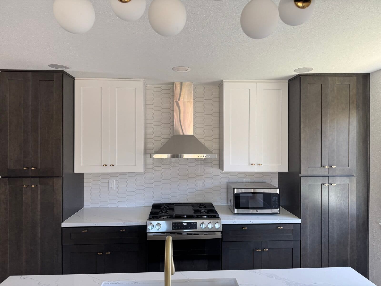 Range wall with white upper cabinets, stainless hood, gas range, and white elongated-hex tile backsplash