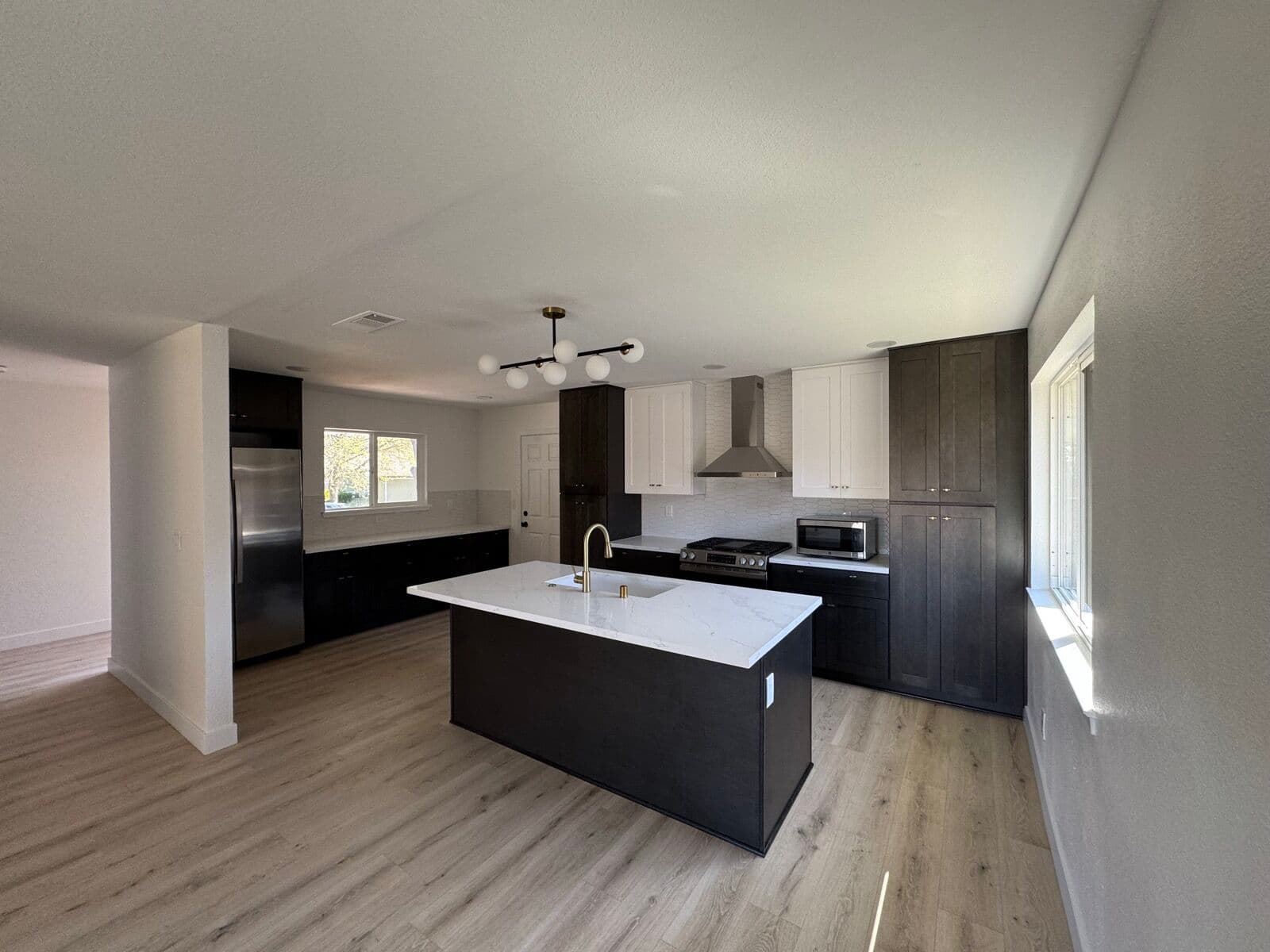 Wide view of the open kitchen and living area with island, chandelier, and wide-plank flooring