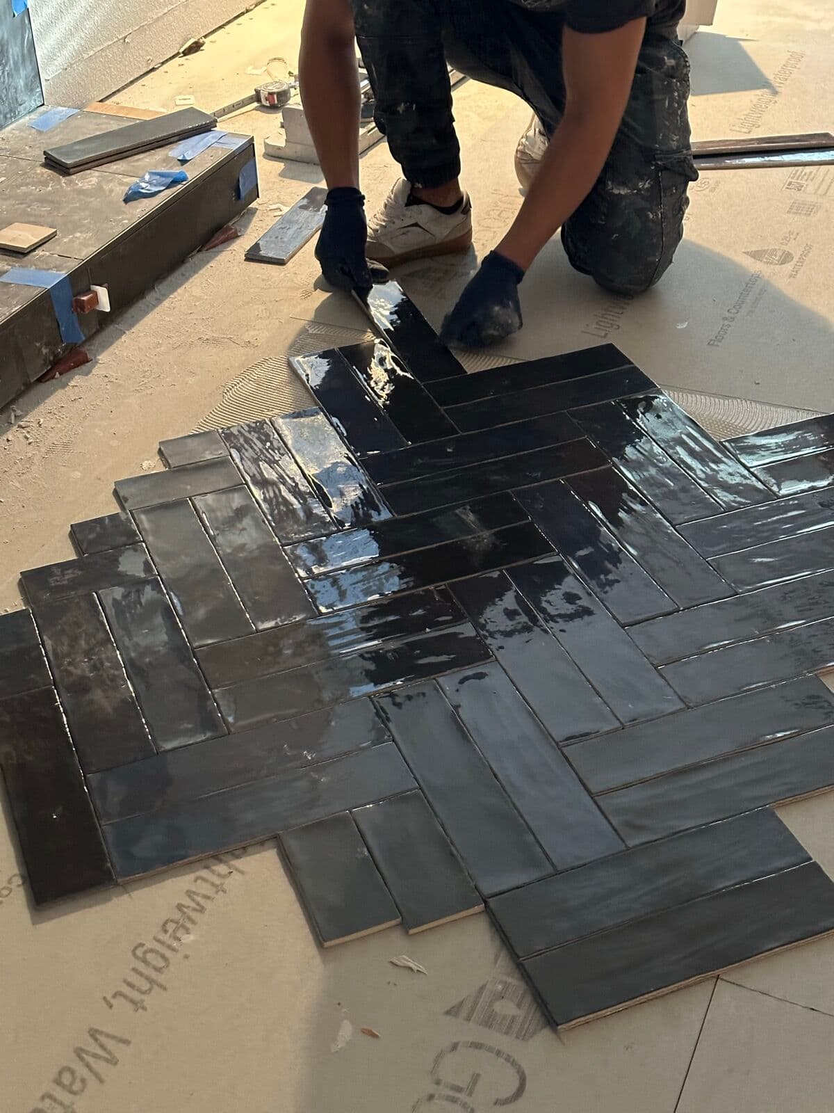 Tile setter laying glossy charcoal tile in a herringbone pattern during the fireplace surround install