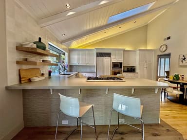 Finished kitchen with gray quartz bar peninsula, gas cooktop, floating oak shelves, and vaulted plank ceiling with skylight