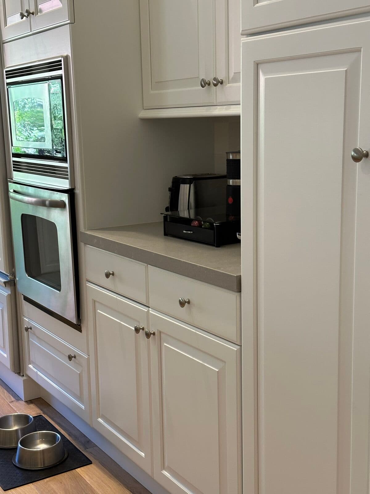 Stainless double wall oven and microwave set into white raised-panel cabinets beside a quartz landing counter