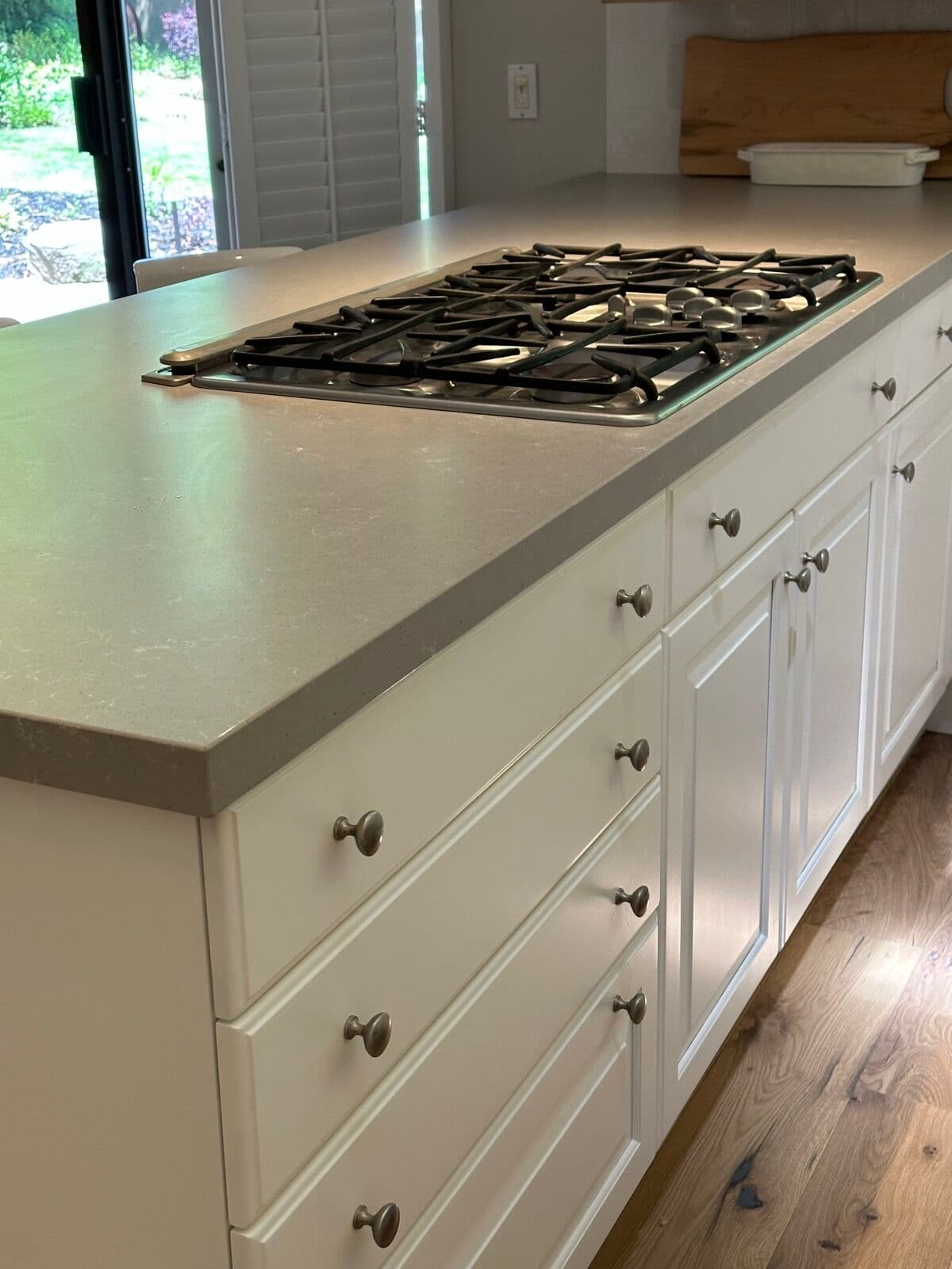 Close-up of the island corner showing gray quartz countertop edge, white drawer fronts, and brushed-nickel knobs