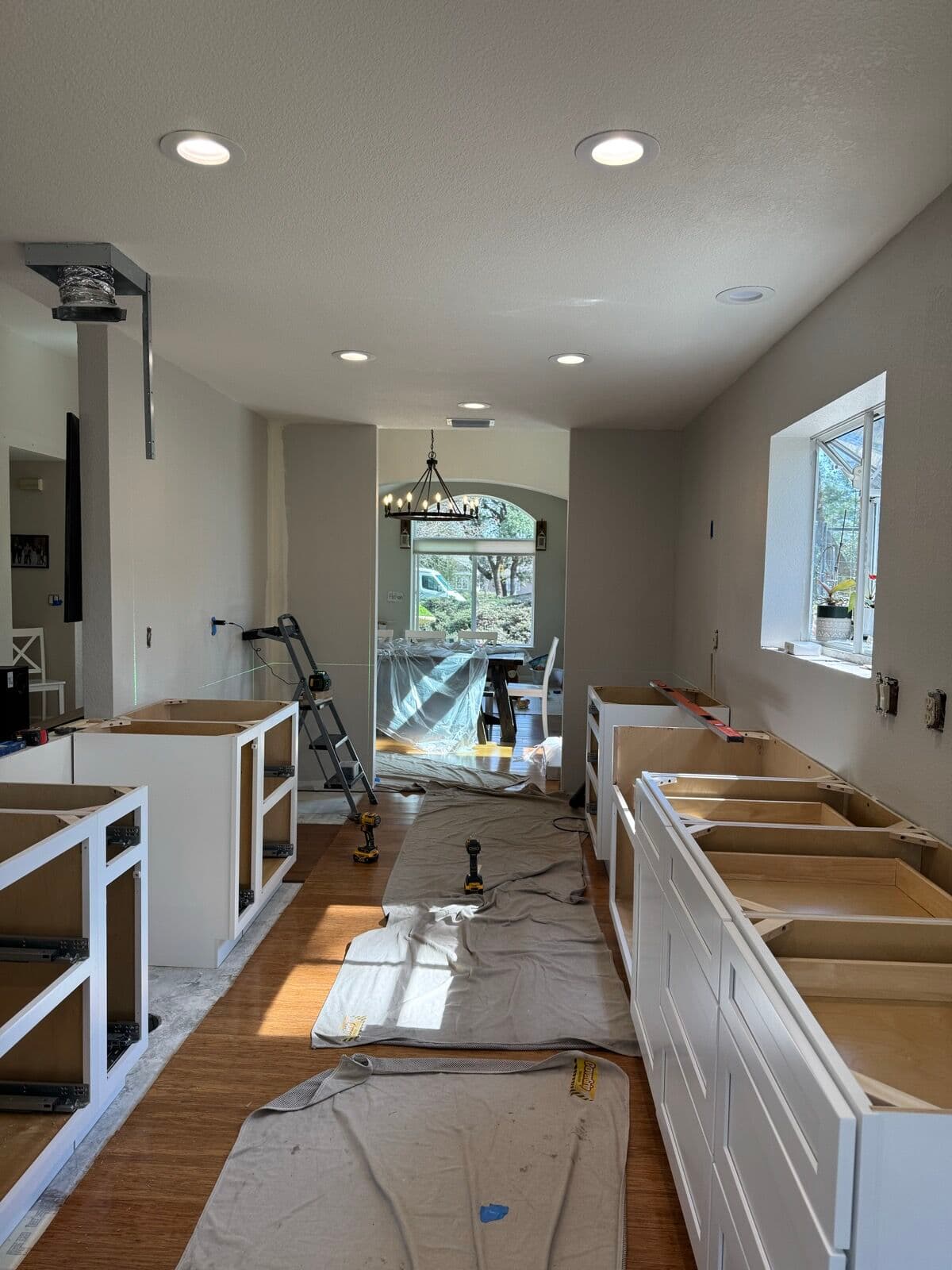 Island and wall base cabinet frames during assembly with a step ladder and level in a galley kitchen