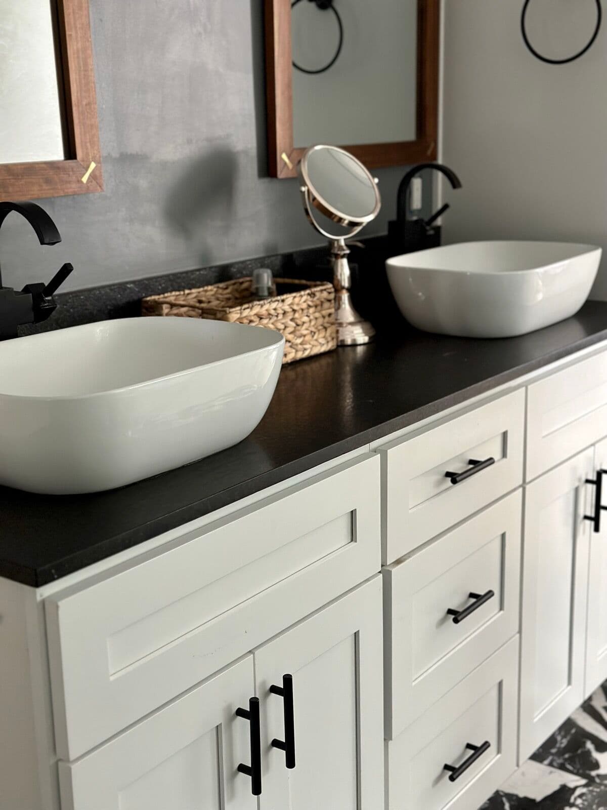 White shaker double vanity with honed black countertop, two white vessel sinks, matte black faucets, and wood-framed mirrors
