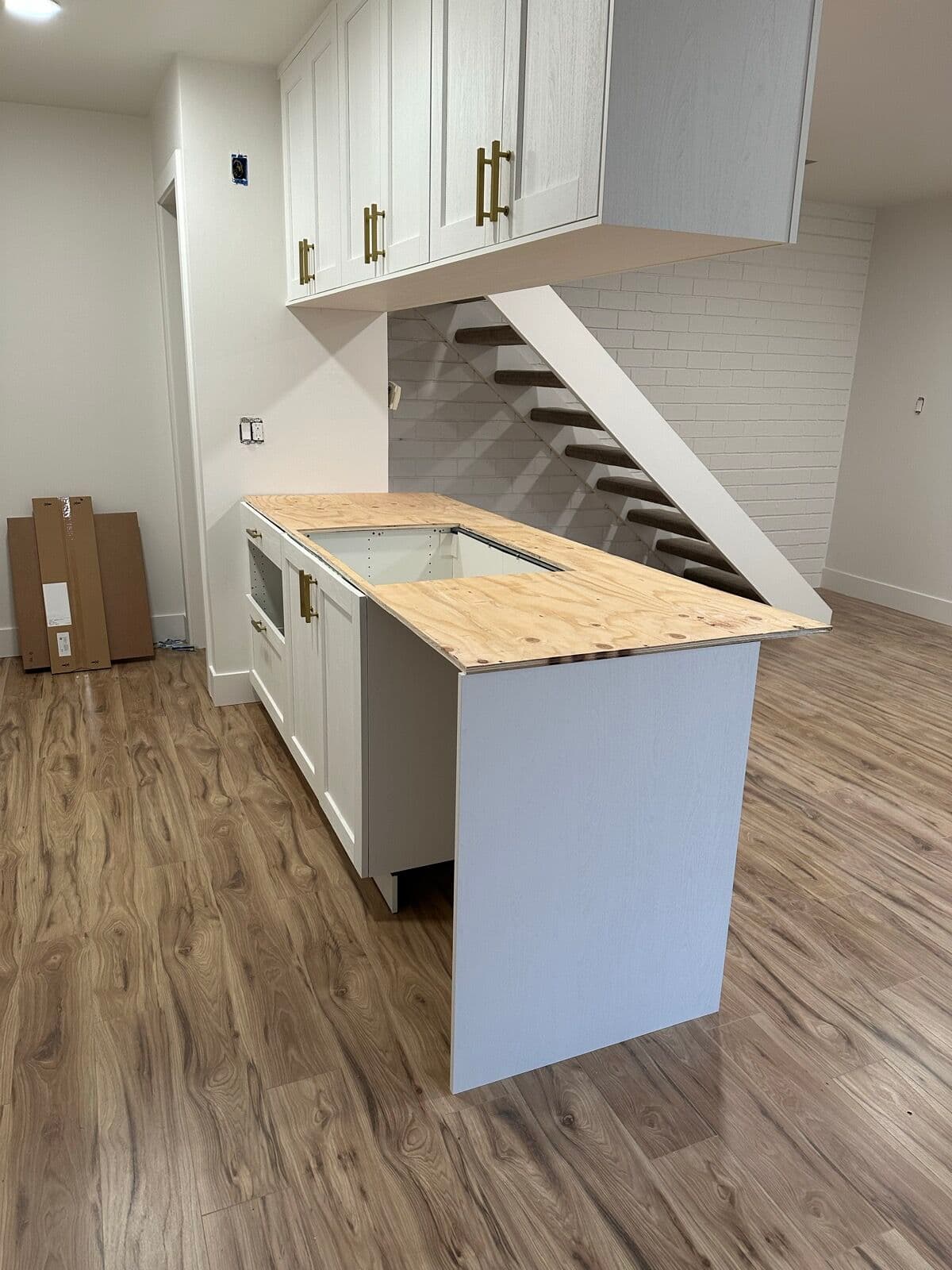 Before — Kitchen peninsula by the floating stairs: mid-build with cabinets set and a plywood sub-top cut for the cooktop, finished with white quartz and the cooktop installed.