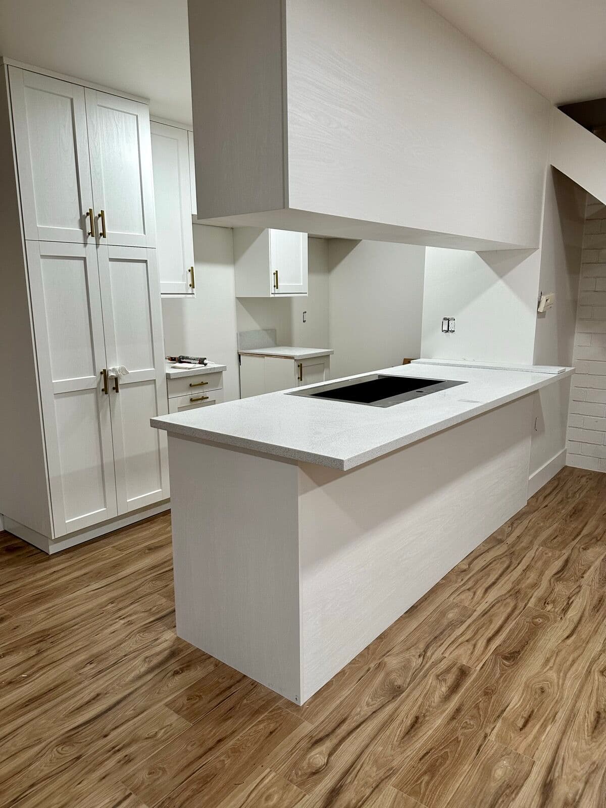 Compact condo kitchen with white shaker cabinets, brass pulls and a white quartz peninsula