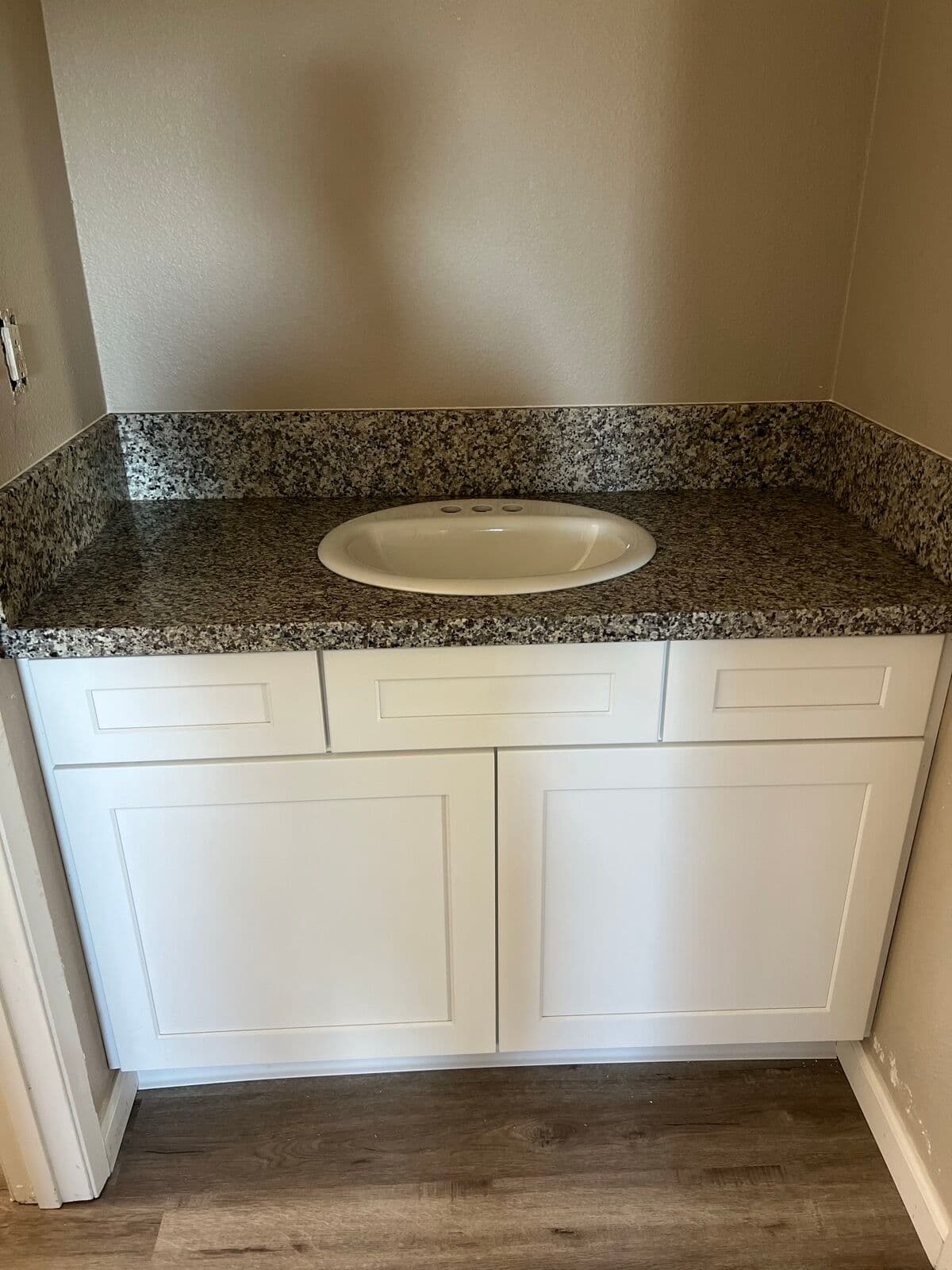 White shaker vanity with a speckled granite top and matching backsplash