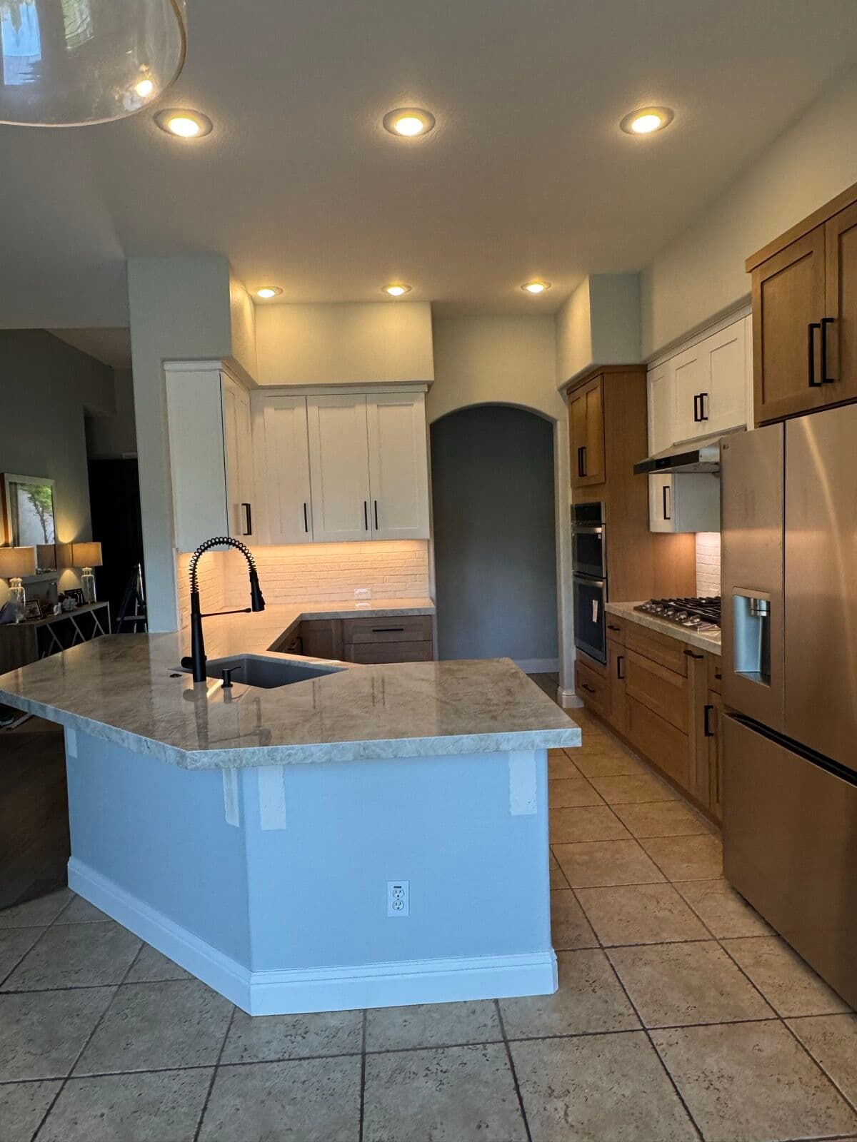 Wide view of the remodeled Folsom kitchen with stone-top island, white and oak shaker cabinets, and arched doorway