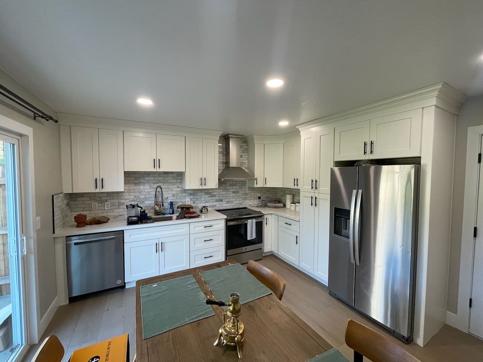 Finished kitchen with white shaker cabinets, marble brick backsplash, stainless appliances, and a chimney range hood