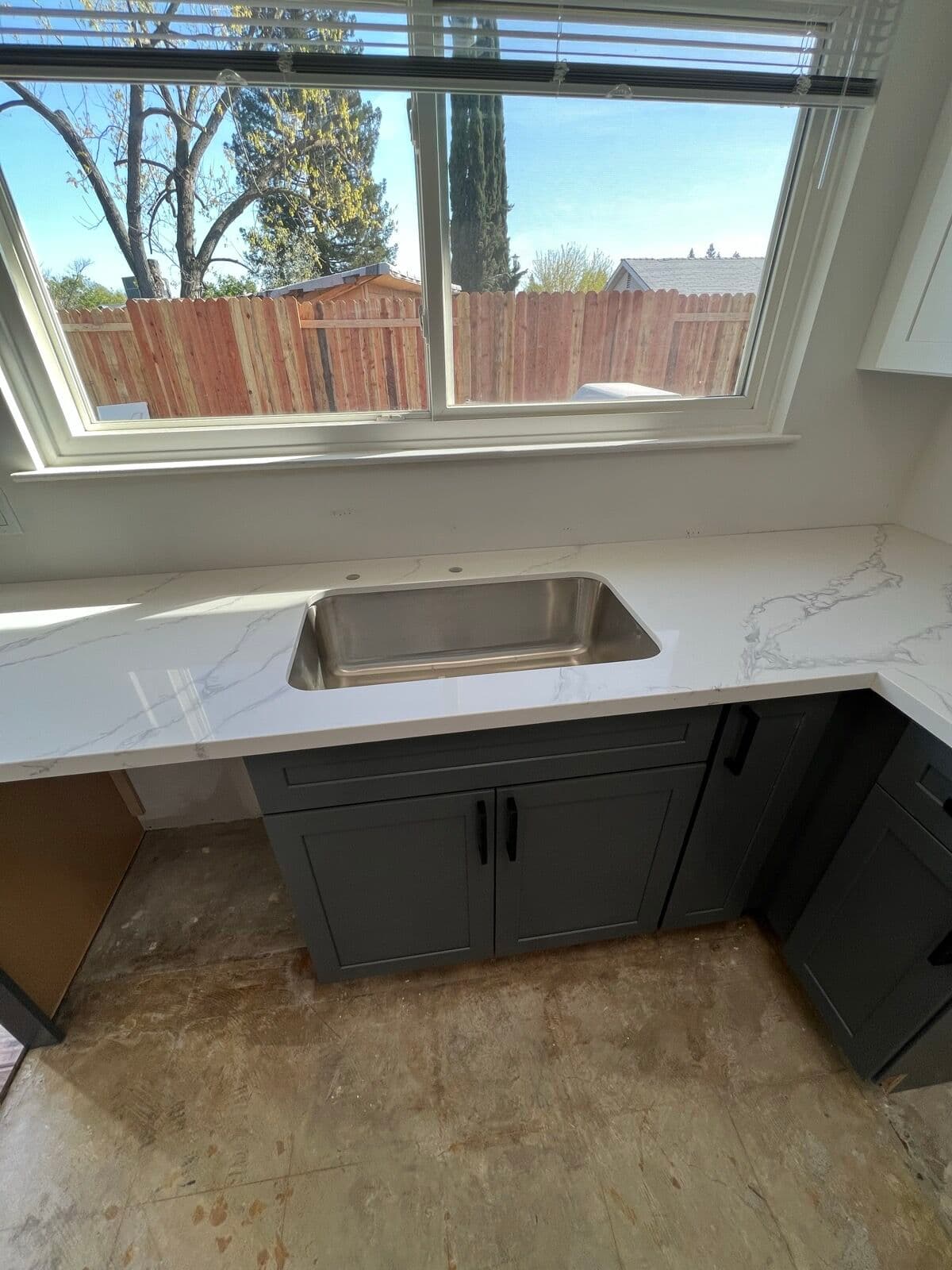 Stainless undermount sink set into a marble-look countertop before the floor went down