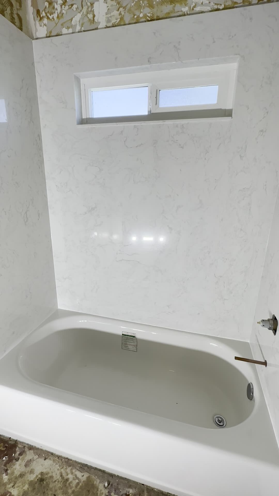 New white marble-look surround panels around an alcove bathtub with a small horizontal window
