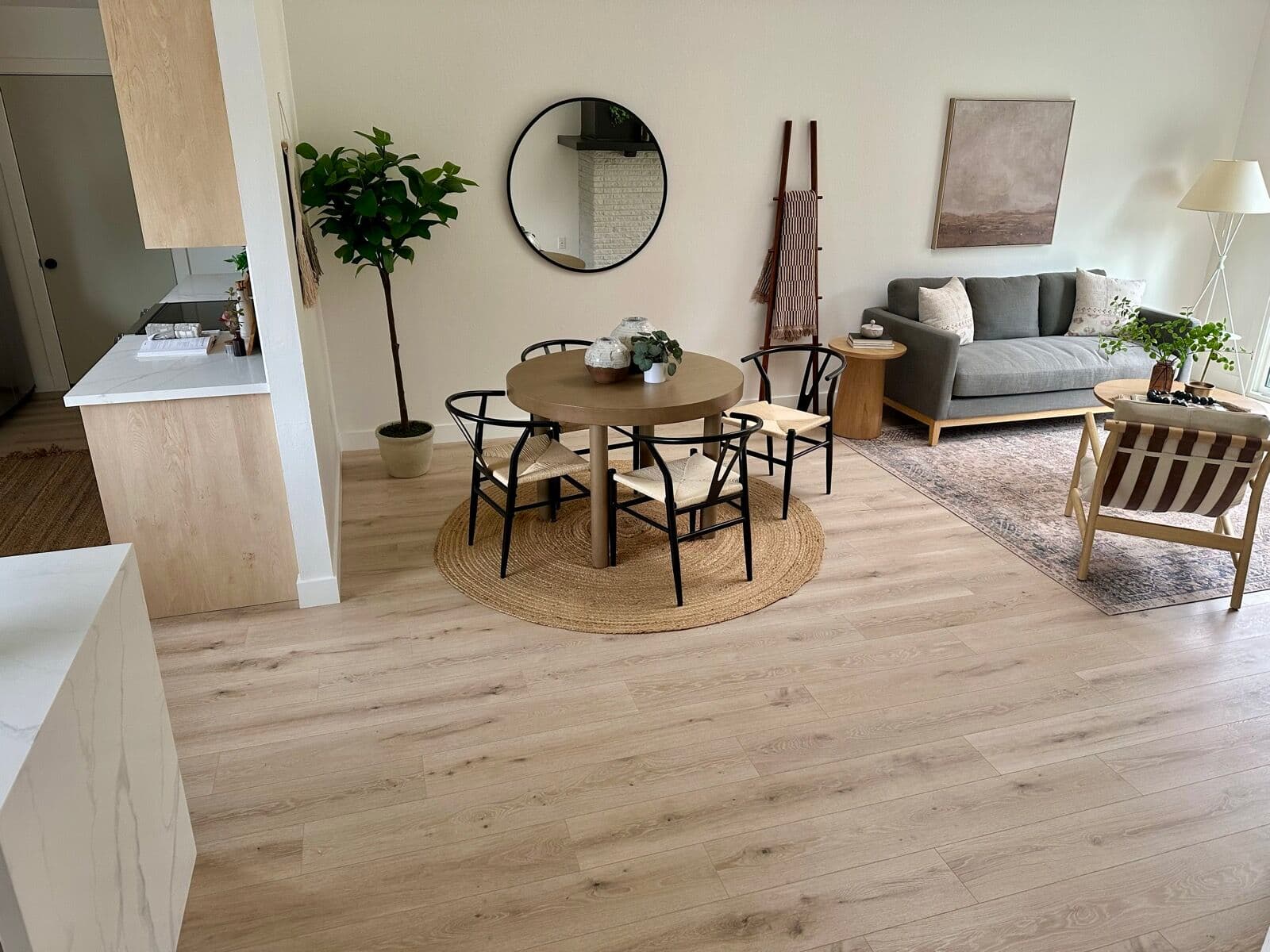 Wide-plank light wood-look flooring through a staged dining and living area