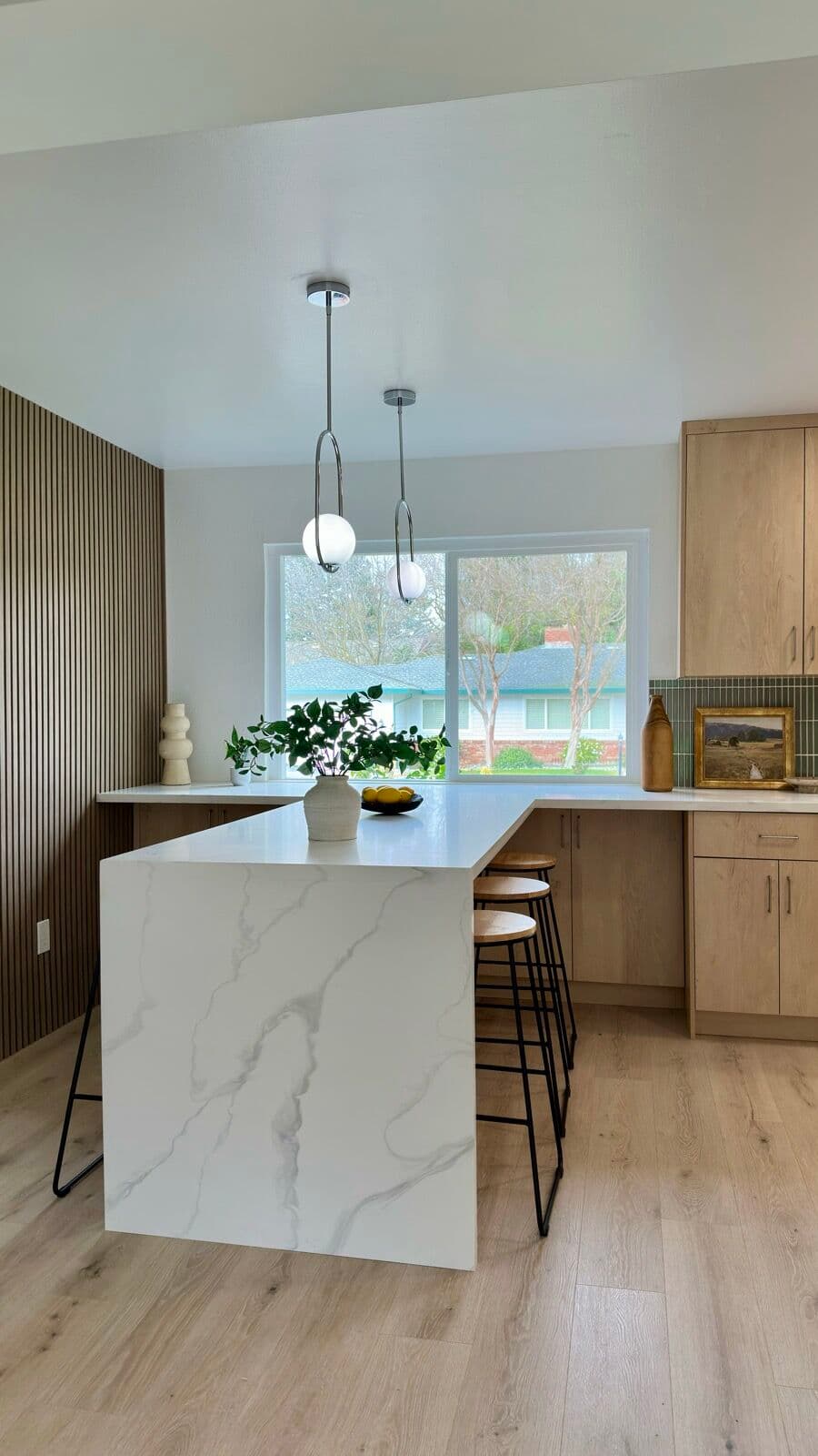 Marble-look island under chrome globe pendants with white-oak cabinets behind